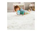 Toddler in pajamas drinking from a sippy cup while lying on a white rug.