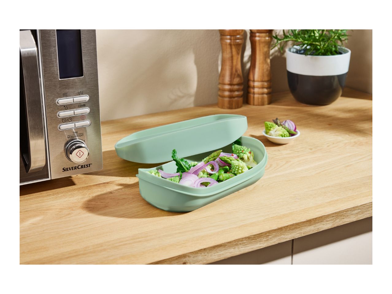 A SilverCrest microwave and a light green steamer filled with vegetables on a wooden counter.
