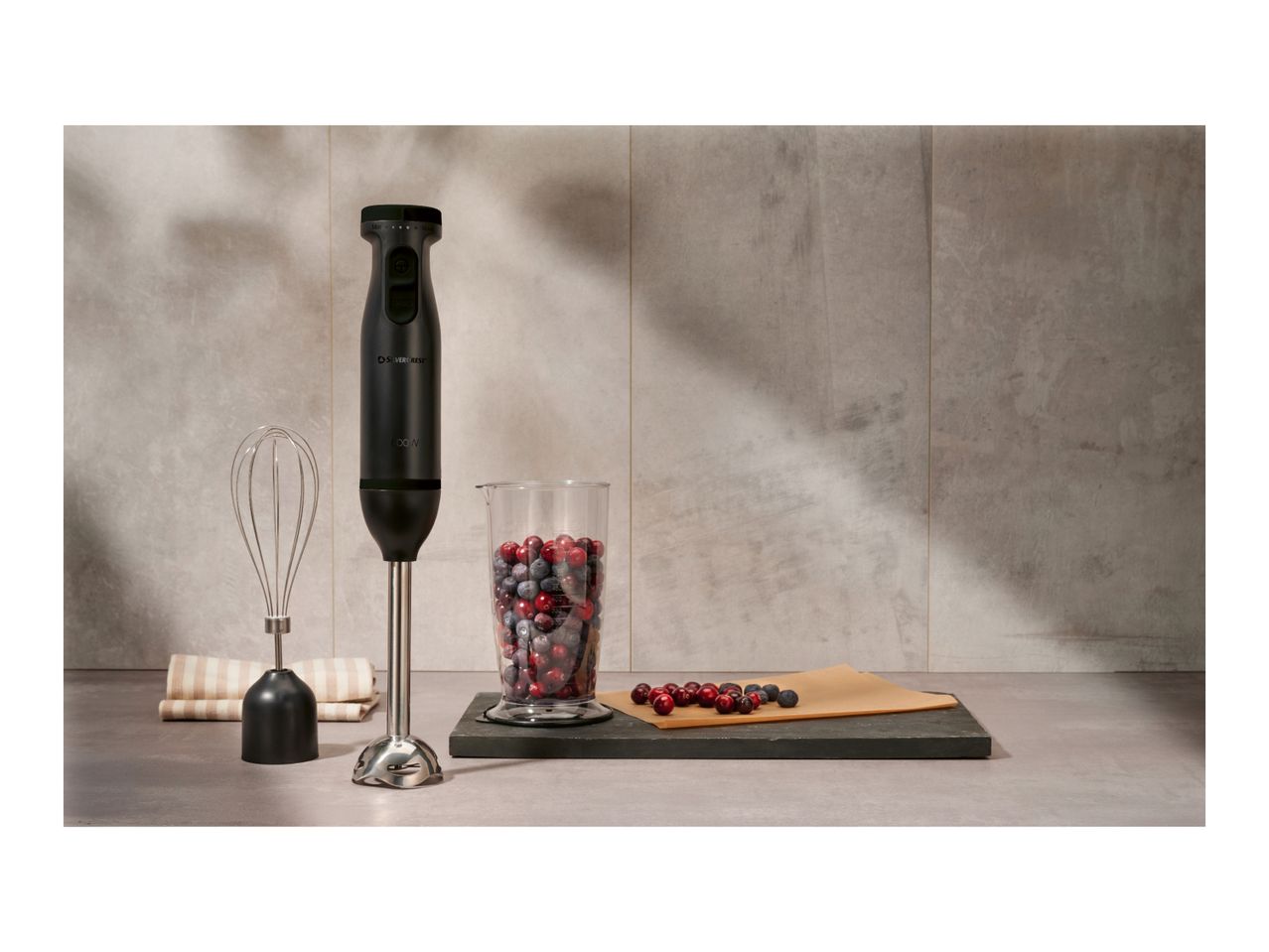 Silvercrest hand blender with whisk, measuring cup of berries, and berries on a board.