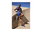 Man in blue athletic wear and running vest, leaning against a concrete wall.