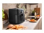 Black air fryer on a kitchen counter with sweet potato fries and ingredients.