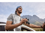Homem de t-shirt CRIVIT e binóculos, a observar a paisagem montanhosa.