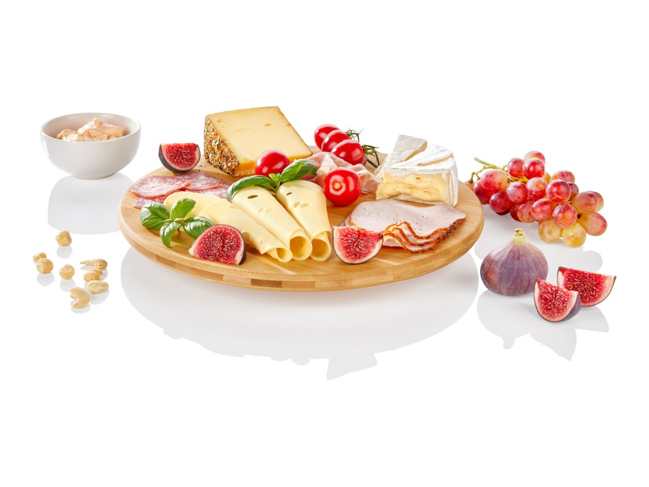 A round bamboo cheese board displays various cheeses, figs, and grapes.