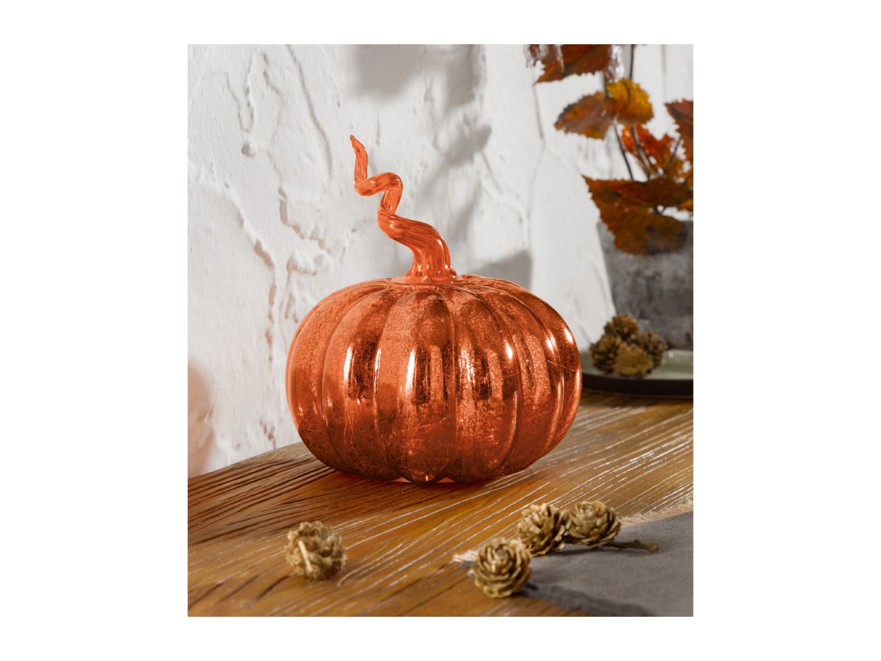 A shiny orange pumpkin decoration with a curly stem on a wooden surface.