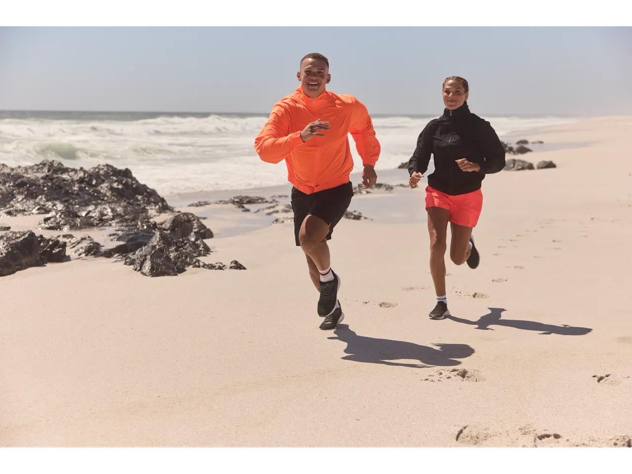 Doi oameni alergând pe plajă în ținută sportivă.