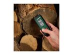 A hand holds a Parkside moisture meter against a stack of firewood, showing a 0.0% concrete reading.