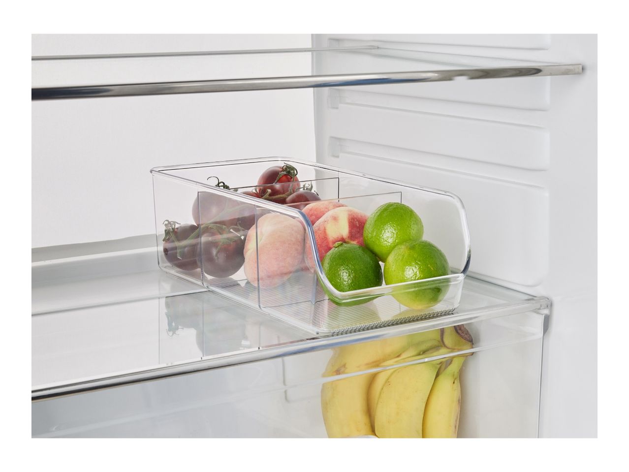 Clear fridge organizer with tomatoes, peaches, and limes, bananas below.