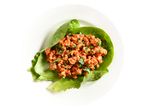 Lettuce wraps with minced meat filling, garnished with fresh herbs on a white plate.