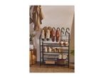 Black metal shoe rack with various shoes, a jacket, and a plant in a neutral-toned room.