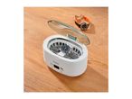 Ultrasonic cleaner with a watch inside, placed on a wooden table next to another watch.