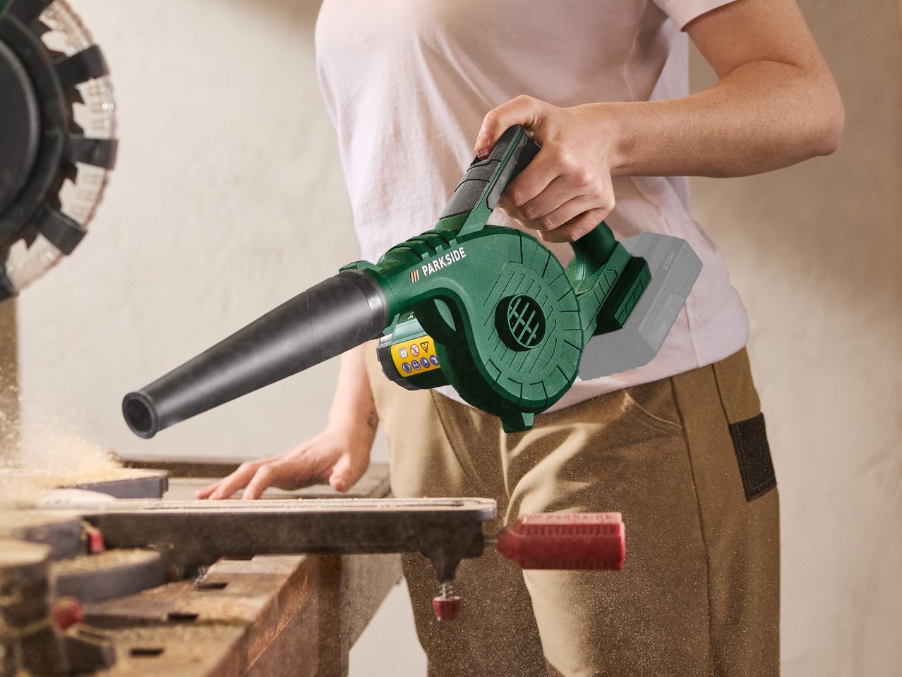 A person uses a cordless leaf blower to clear sawdust from a miter saw.