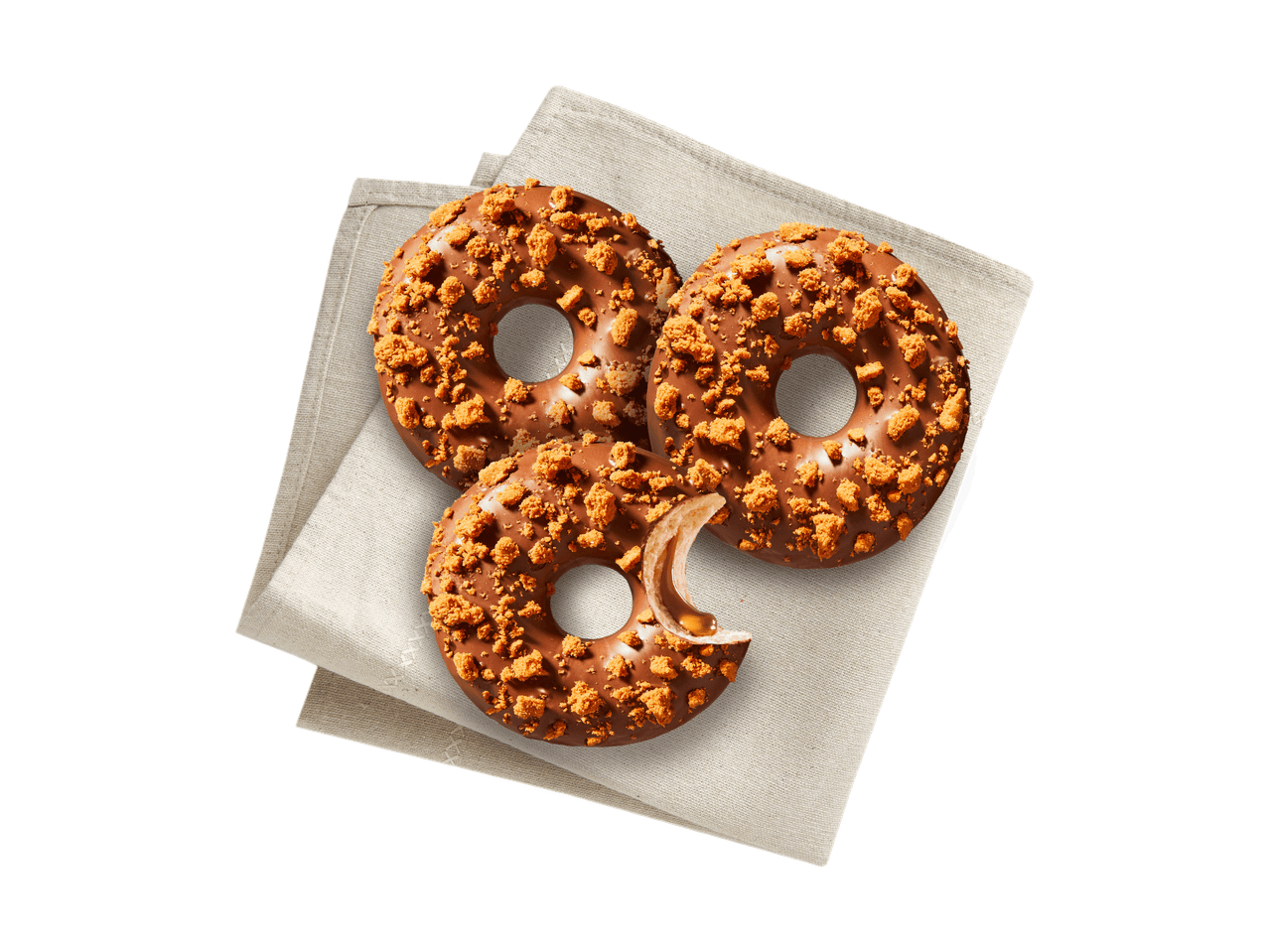 Drei Schoko-Donuts mit Keksstreuseln auf einem beigen Tuch, einer davon angebissen mit Karamellfüllung.