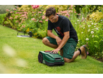Man setting up a robotic lawnmower in a garden with lush greenery and flowers.