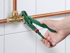 Hand using a green pipe wrench on copper plumbing pipes and brass fittings.