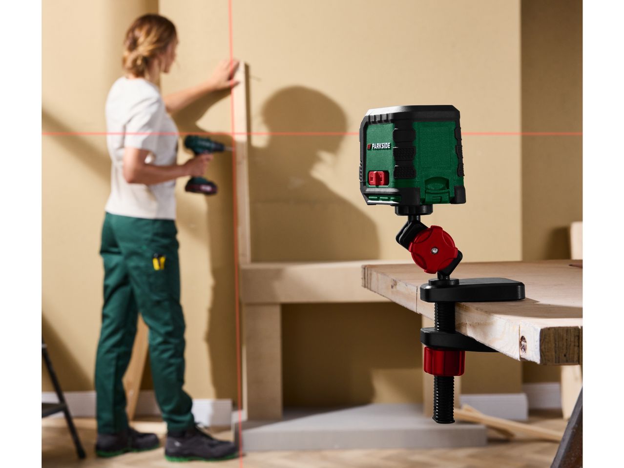 Laser level projecting lines, with a person working on a wall in the background.