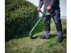 Bărbat folosind un trimmer de gazon PARKSIDE pentru a tăia iarba lângă un tufiș.