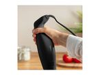 Hand holding a black immersion blender, with tomatoes and a jar in the background.