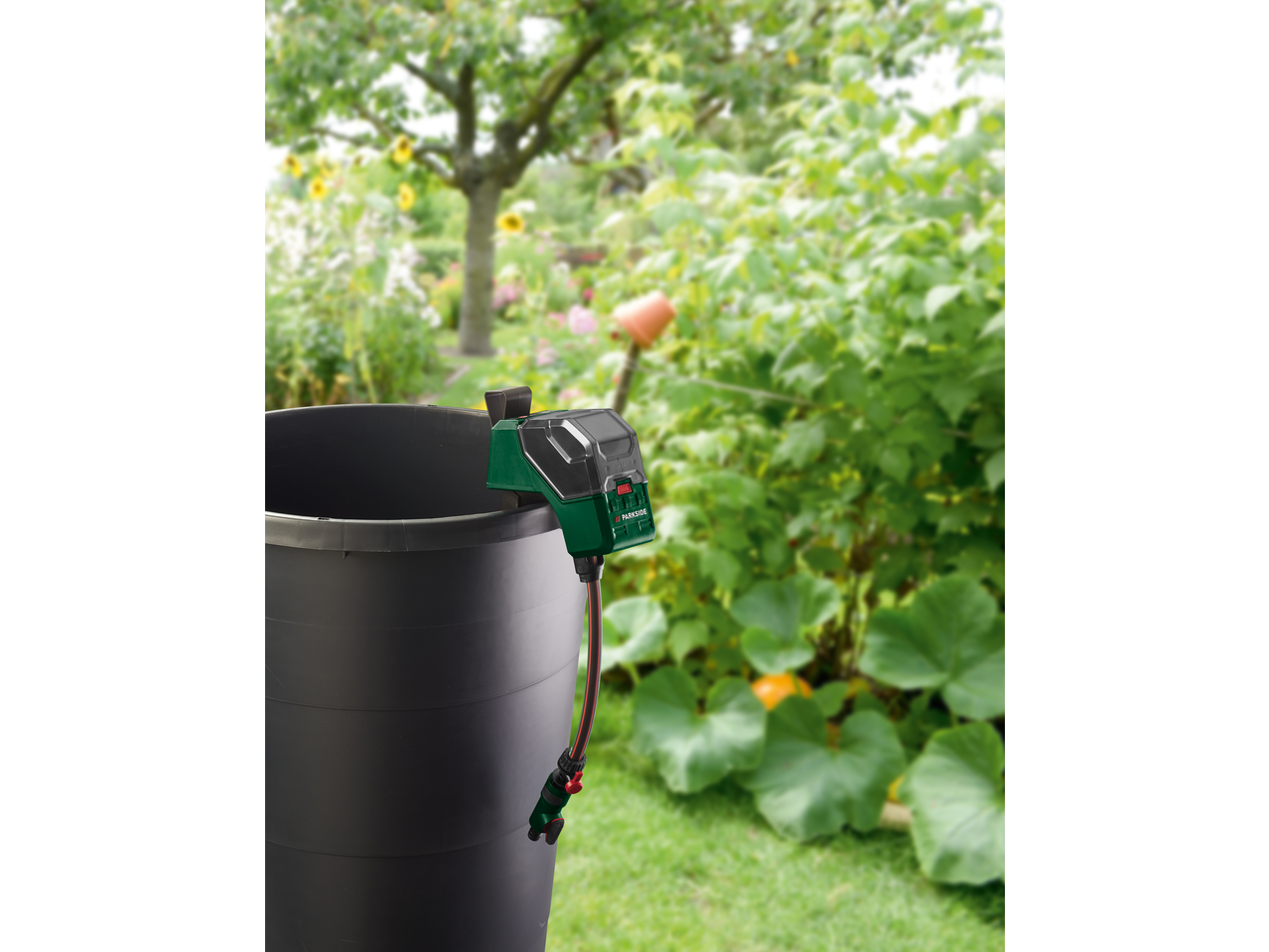 Pompă apă de ploaie PARKSIDE atașată la un butoi negru de ploaie într-un cadru de grădină.