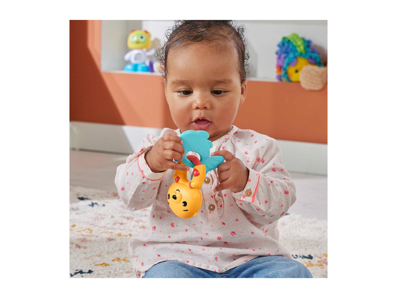A baby playing with a colorful rattle toy, sitting on a patterned rug.