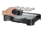 Hand placing the heating element with a temperature dial onto a black electric grill with a metal drip tray.