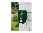Green ultrasonic animal repeller with solar panel mounted on a white brick wall in a garden.