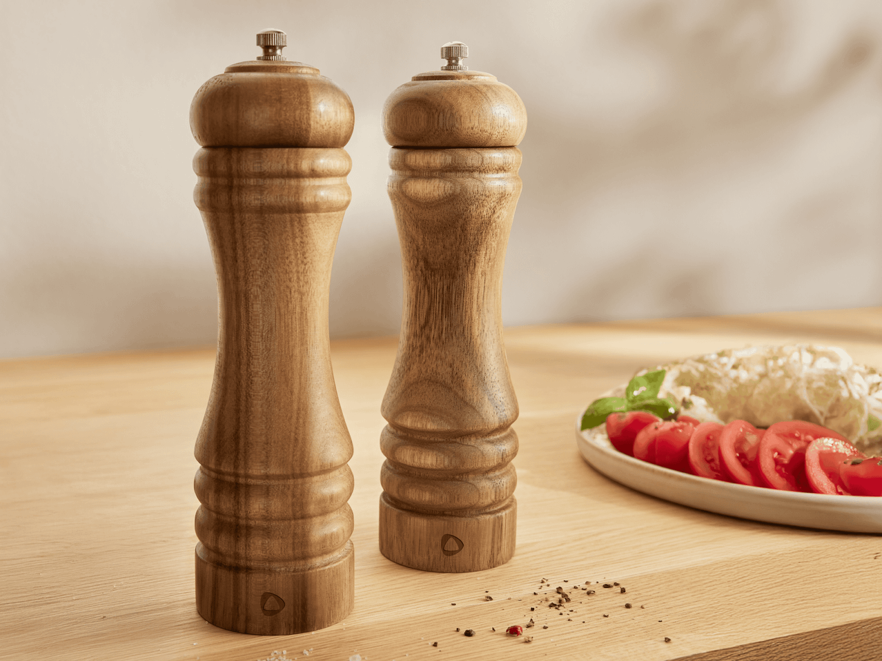 Zwei hölzerne Pfeffer- und Salzmühlen auf einem Holztisch mit Tomaten und Mozzarella.