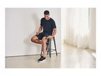 Man in black sportswear using a massage gun on his thigh while sitting on a stool.