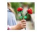 A person holding two red toy roses with green stems and leaves.