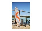 Paddleboard set with board, paddle, pump, and bag on a sandy beach next to a wooden pier.