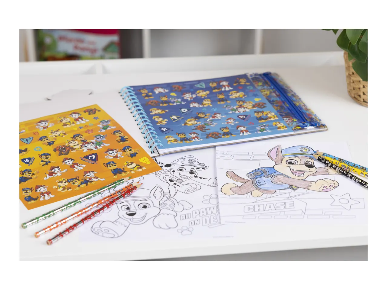 Paw Patrol coloring book, sticker sheet, and pencils on a white table.