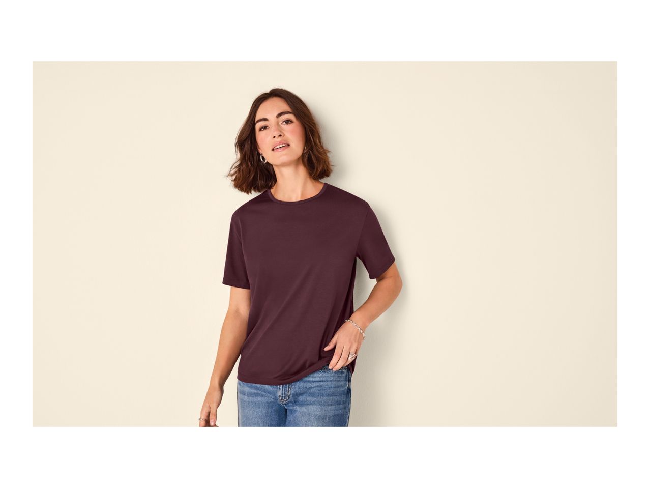 Woman in a dark red t-shirt and blue jeans, posing against a light background.
