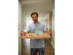 A man carries a tray with two mugs and pastries.