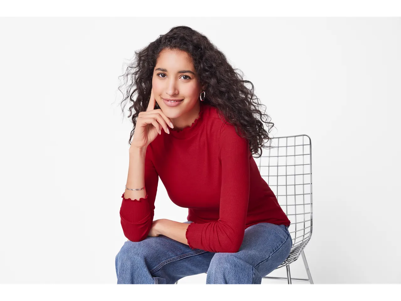 Femeie în bluză roșie rebrată Esmara și blugi, așezată pe un scaun.