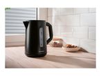 Black electric kettle on a wooden kitchen counter with cookies and a jar in the background.