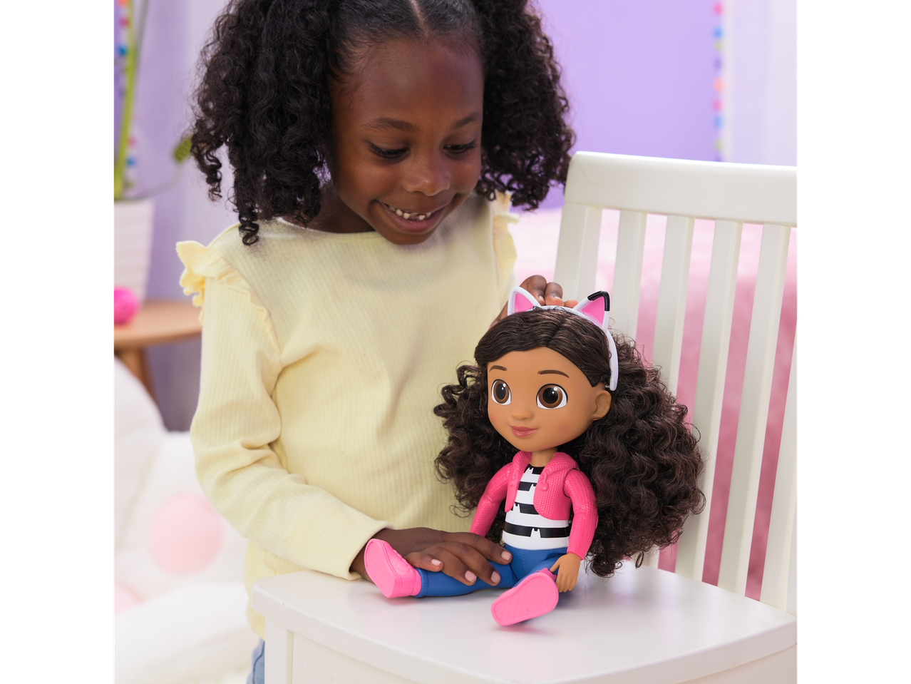 A girl smiling at a Gabby's Dollhouse doll with cat ears