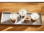 Três copos de macchiato e biscoitos em uma bandeja de cimento.