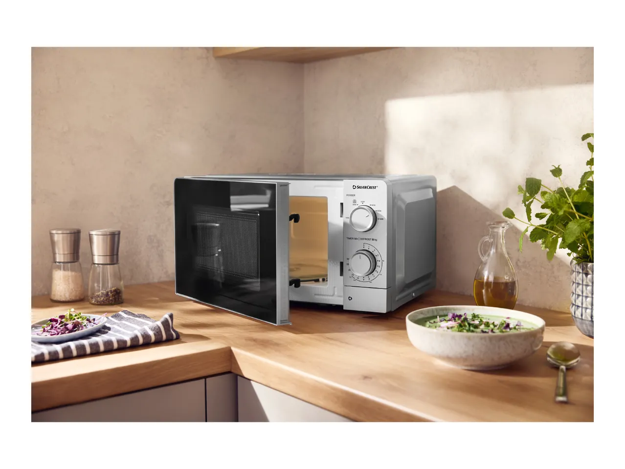 Microwave oven with an open door on a kitchen counter, next to a bowl of soup.