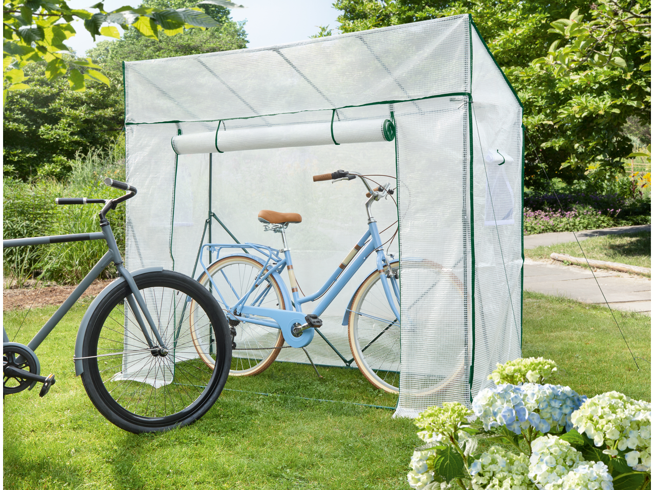 Two bicycles, one blue and one grey, stored inside and next to a transparent bicycle storage tent in a garden.