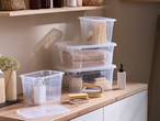 Clear storage boxes with bath and cleaning supplies on a wooden countertop.
