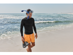 Man in CRIVIT aqua shoes, rash guard, and snorkel mask walking on a beach.