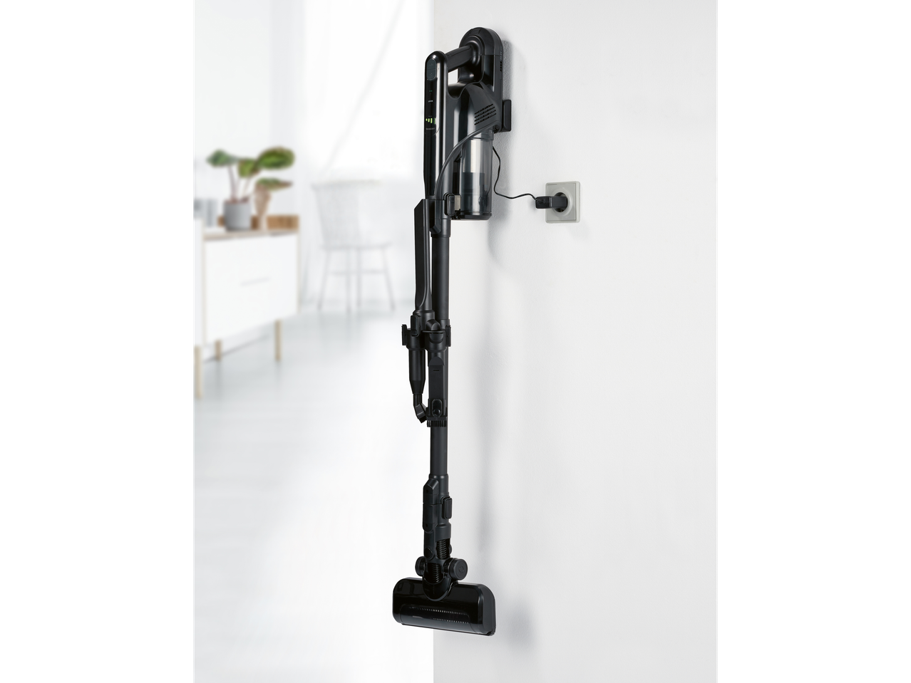 A black cordless stick vacuum cleaner is charging on a wall mount.