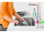 A woman washes a pot in the kitchen with a sponge.