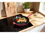 Un piatto di salmone e verdure che cuoce in una padella in ghisa rossa su un piano cottura a induzione nero.