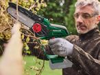 A man prunes branches with a Parkside mini chainsaw, wood chips flying.