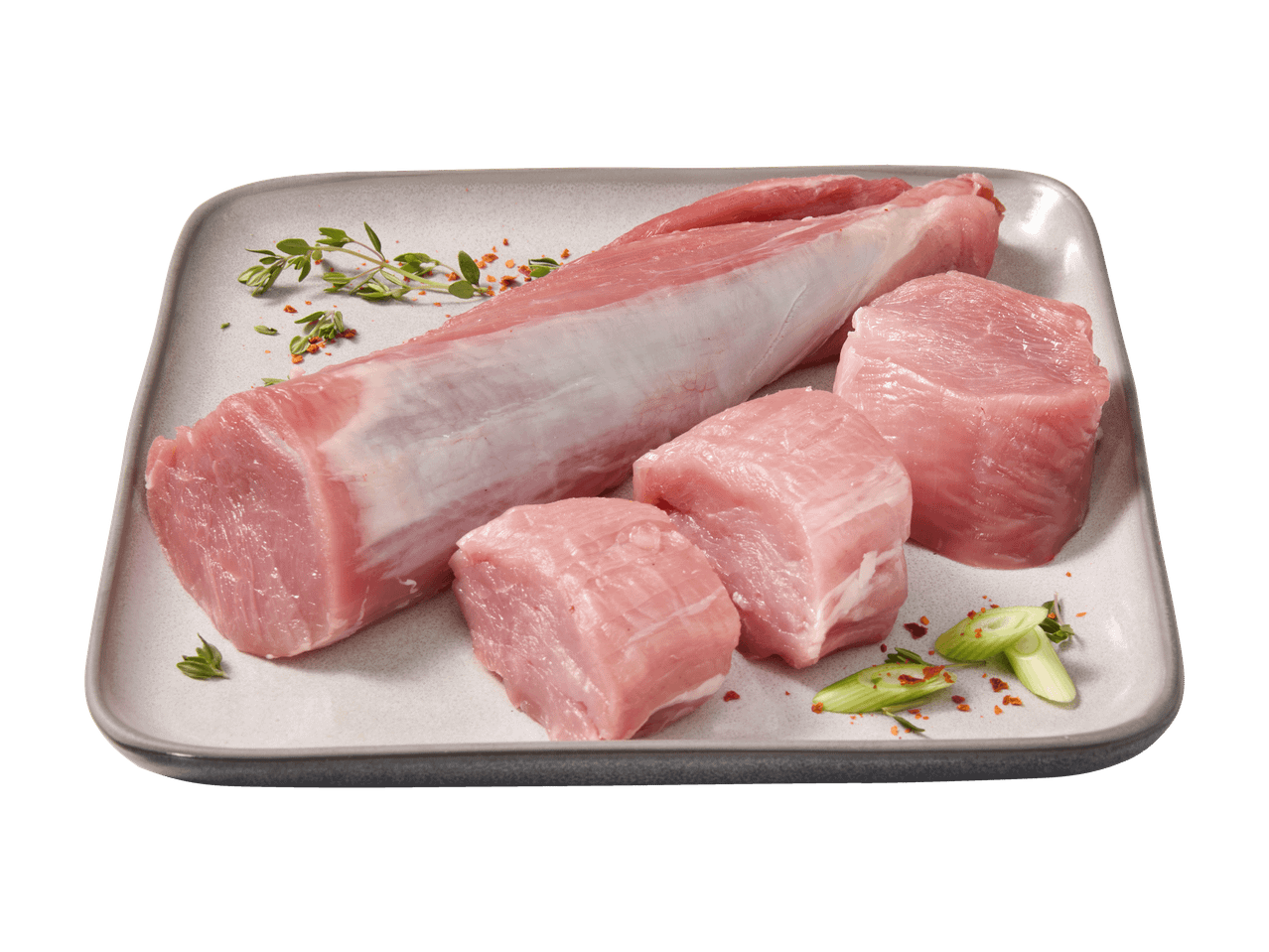 Filet de porc cru et morceaux de porc coupés en dés sur une assiette avec des herbes.