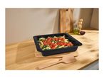 Pasta bake with tomatoes and spinach in a black baking dish on a wooden counter.