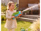 Smiling girl playing with a water blaster in a sunny garden.