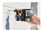 A person drilling into a white brick wall with a cordless rotary hammer drill.