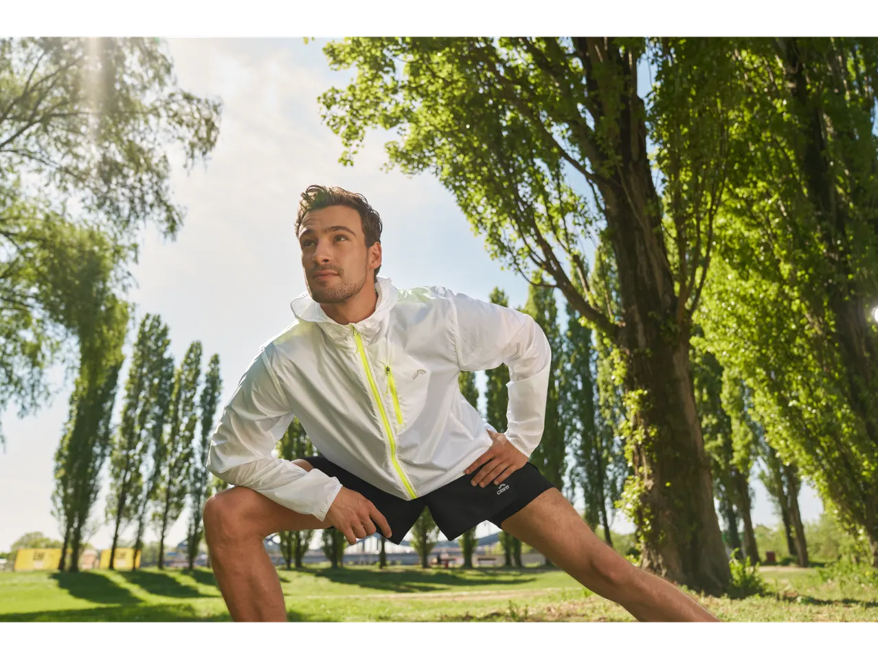 Un bărbat cu o jachetă sport Crivit se întinde într-un parc.