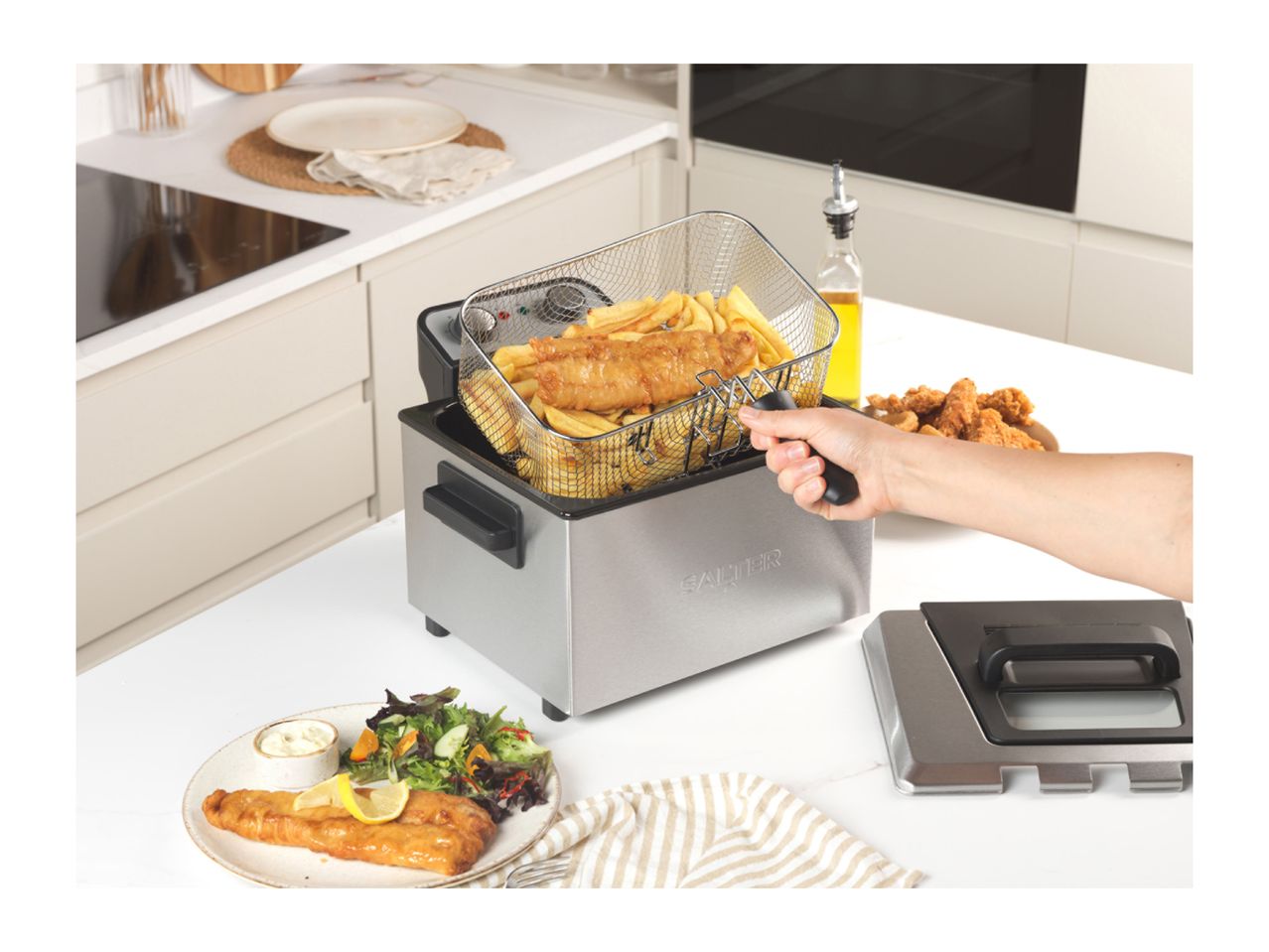 A person lifting a basket of fish and chips from a Salter deep fryer in a kitchen.